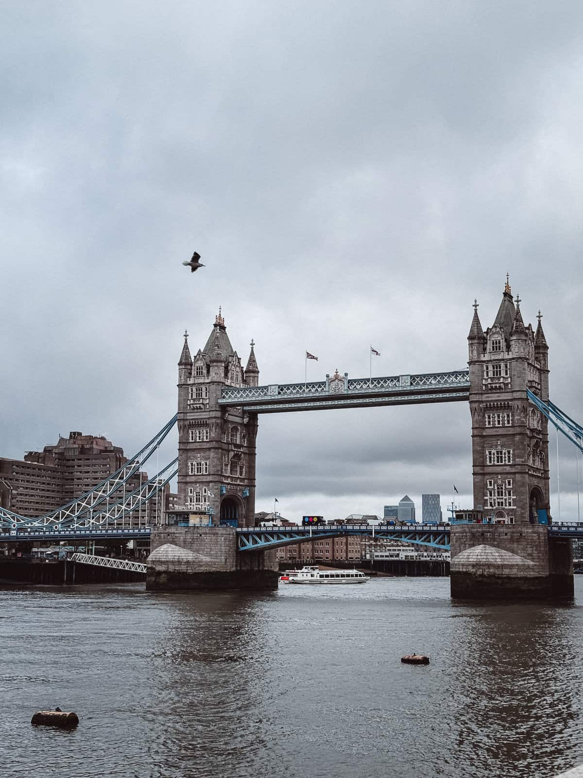  The iconic Tower Bridge in London on an overcast day, with its majestic towers and blue accents, as a boat passes underneath and a bird soars above, symbolizing the enduring splendor of this historic city.