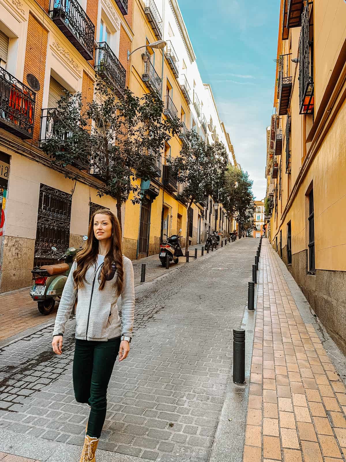 A woman walks down a cobblestone street in Madrid with yellow buildings