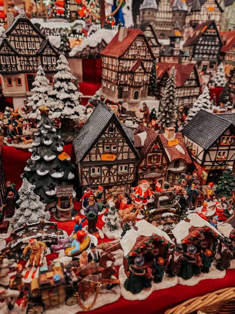 A miniature winter village scene complete with snow-covered houses, figures, and trees, on display at a Christmas market.
