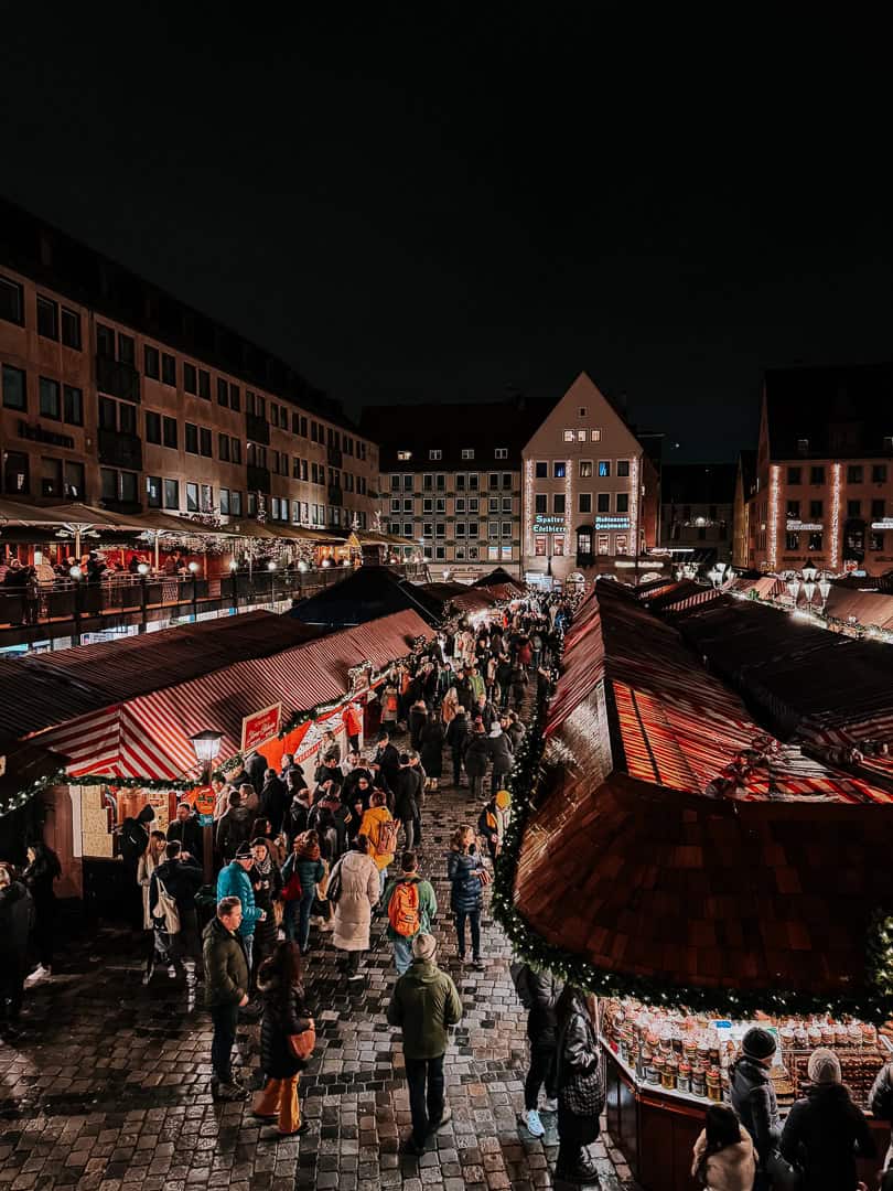 Aerial view of Nuremberg's Christmas market at night, showcasing the busy crowd and the festive stalls with twinkling lights.
