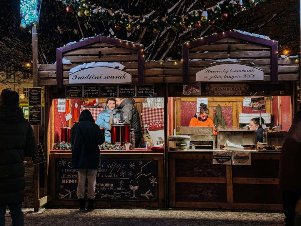 An evening scene at a Christmas market where vendors serve steaming beverages from a traditional 