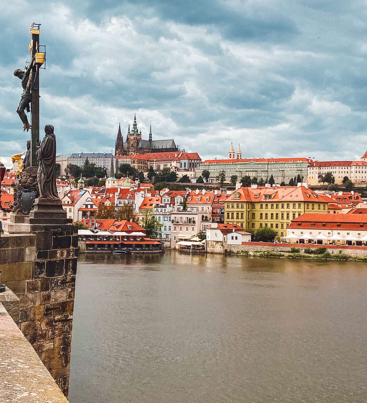 A statue on the Charles Bridge stands watch over the Vltava River, with Prague Castle rising majestically in the background, capturing the historical and cultural grandeur of Prague.