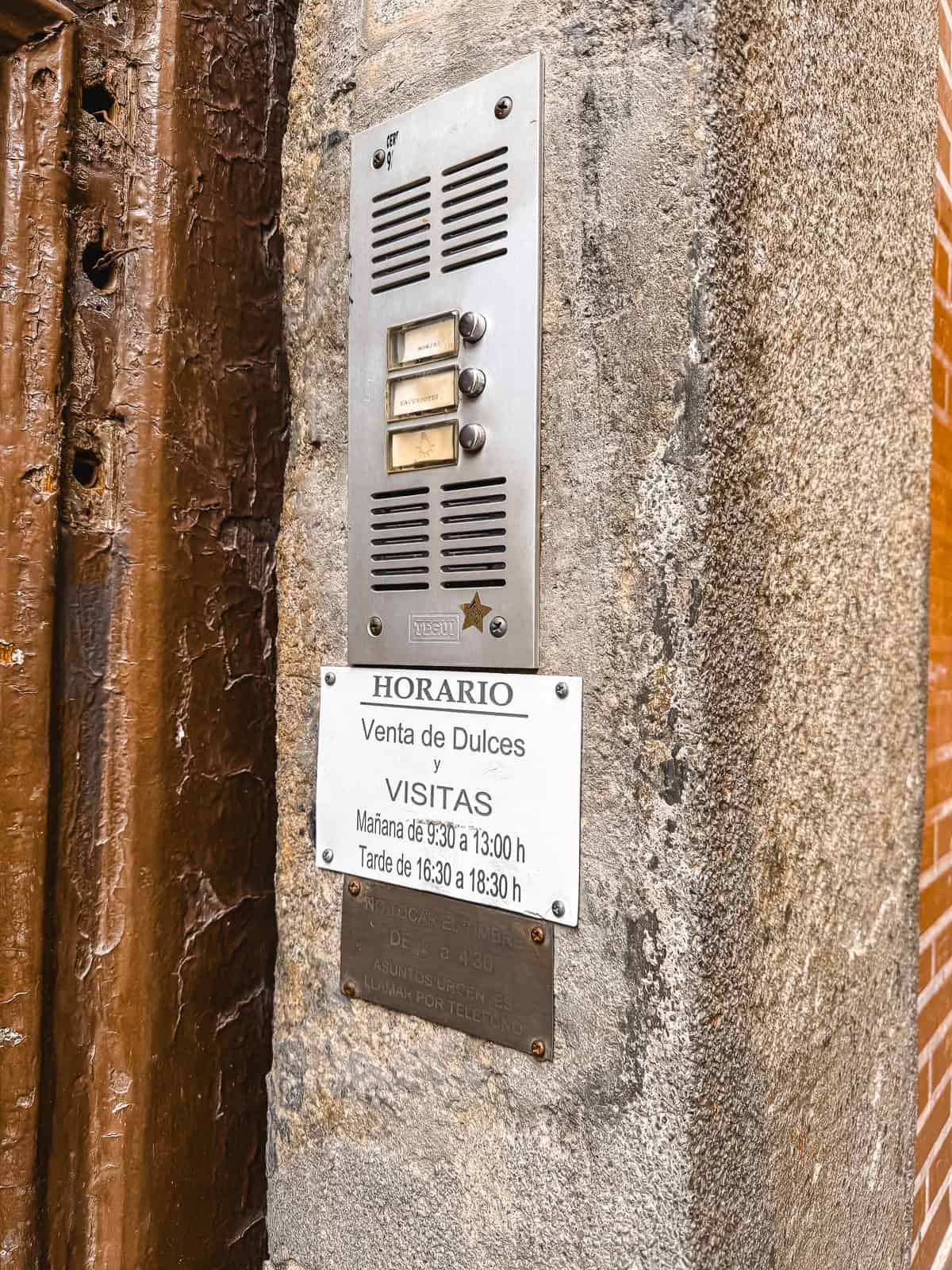 Close-up of a weathered signage plaque reading 'HORARIO Venta de Dulces y VISITAS' beside a door entry intercom system on a textured stone wall
