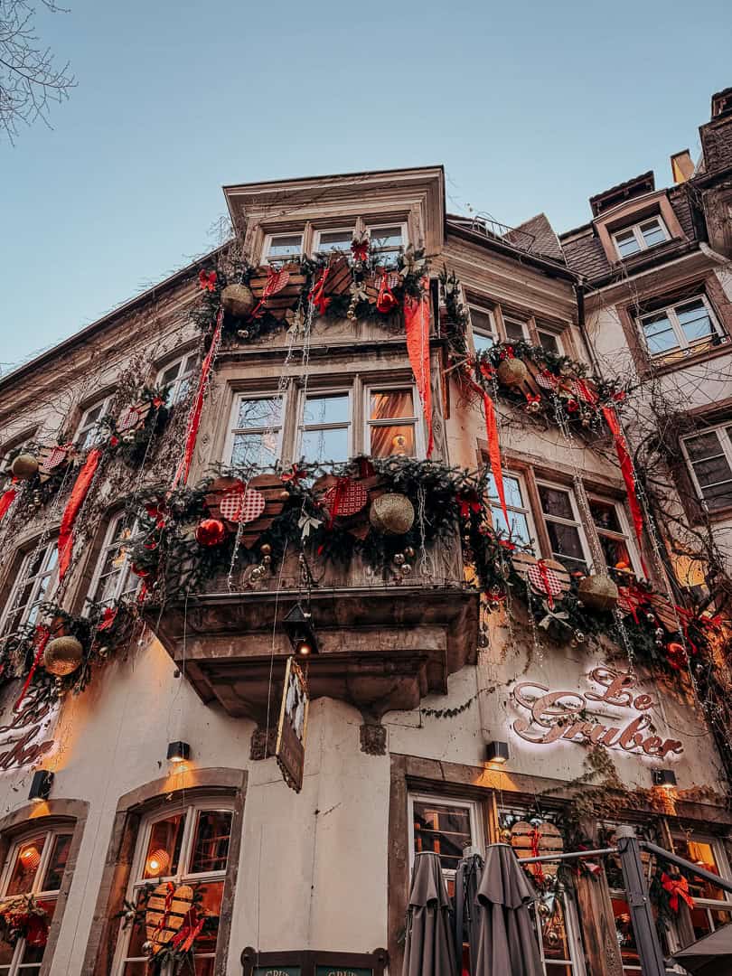 A traditional wooden half-timbered house, beautifully decorated with Christmas wreaths and ornaments, with a restaurant entrance invitingly open to passersby.