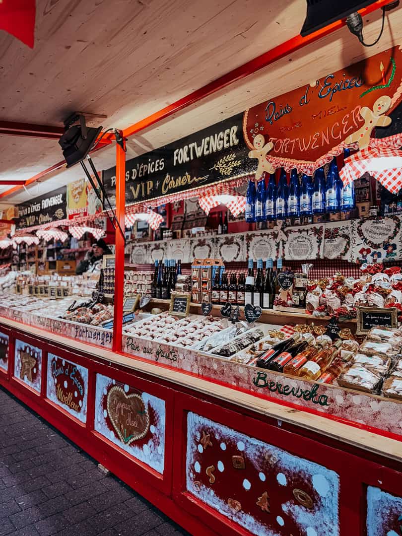 A festive market stall in Strasbourg is filled with gingerbread and assorted regional delicacies under a sign reading 