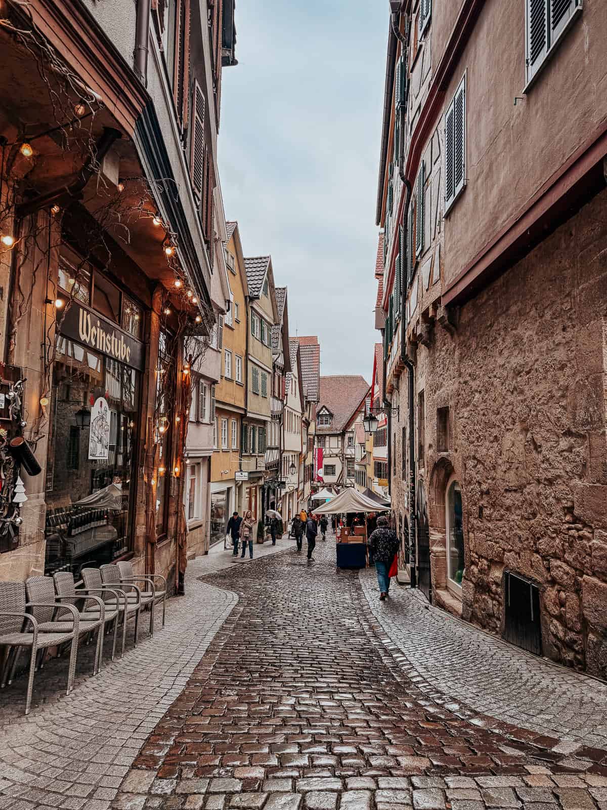 a cute street in Tubingen germany with cobblestones and a few figures walking down it