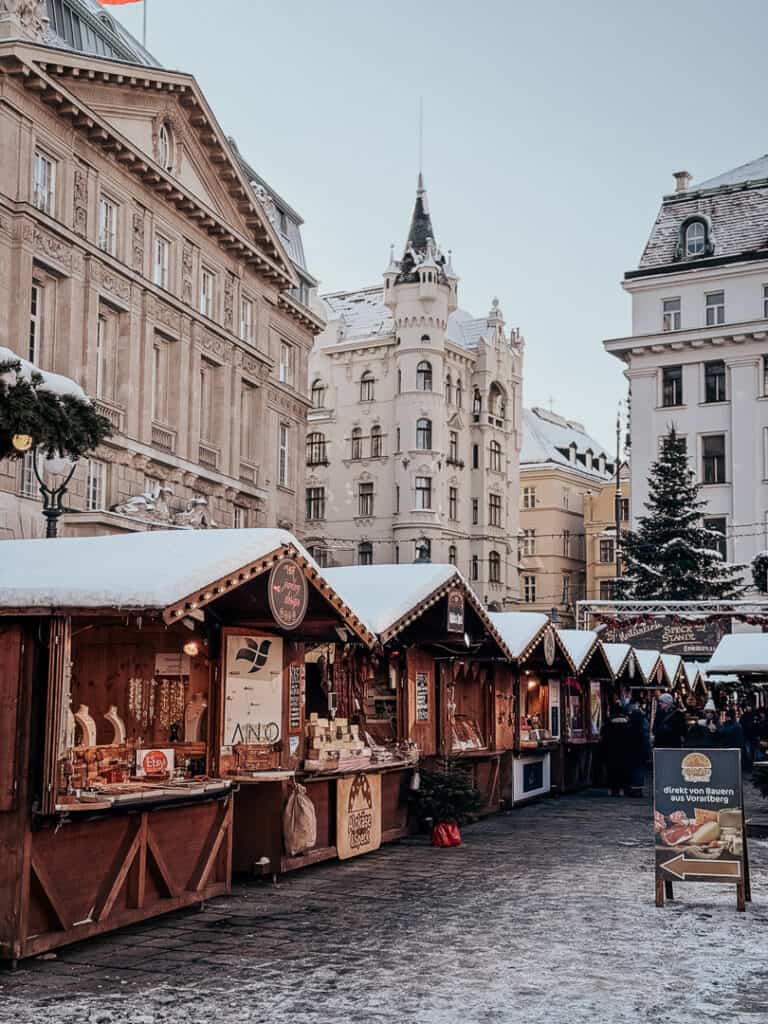 Christmas market stalls with traditional handcrafted goods beneath historic Viennese architecture, frosted with snow