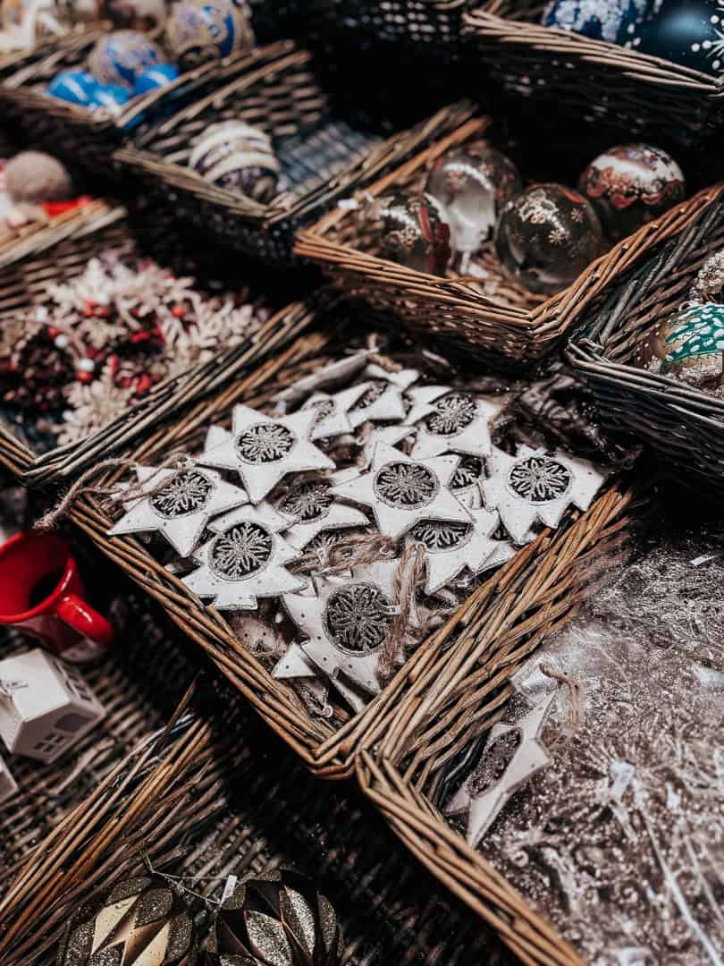 A close-up of beautifully crafted Christmas decorations at a Vienna market, with intricate snowflake designs and other festive ornaments in baskets, dusted with snow.