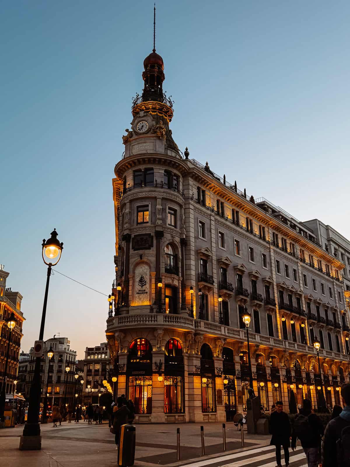 The grandeur of Madrid's architecture is showcased in this image featuring a magnificent building with an elaborate clock tower, illuminated at twilight.