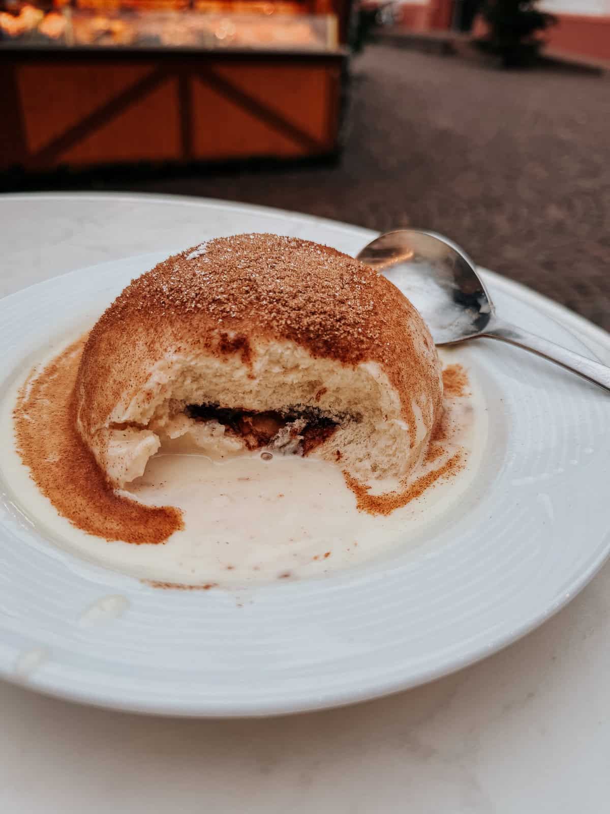 A close-up of a Dampfnudel, a German steamed bun, cut open and served on a white plate with vanilla sauce, sprinkled with sugar.