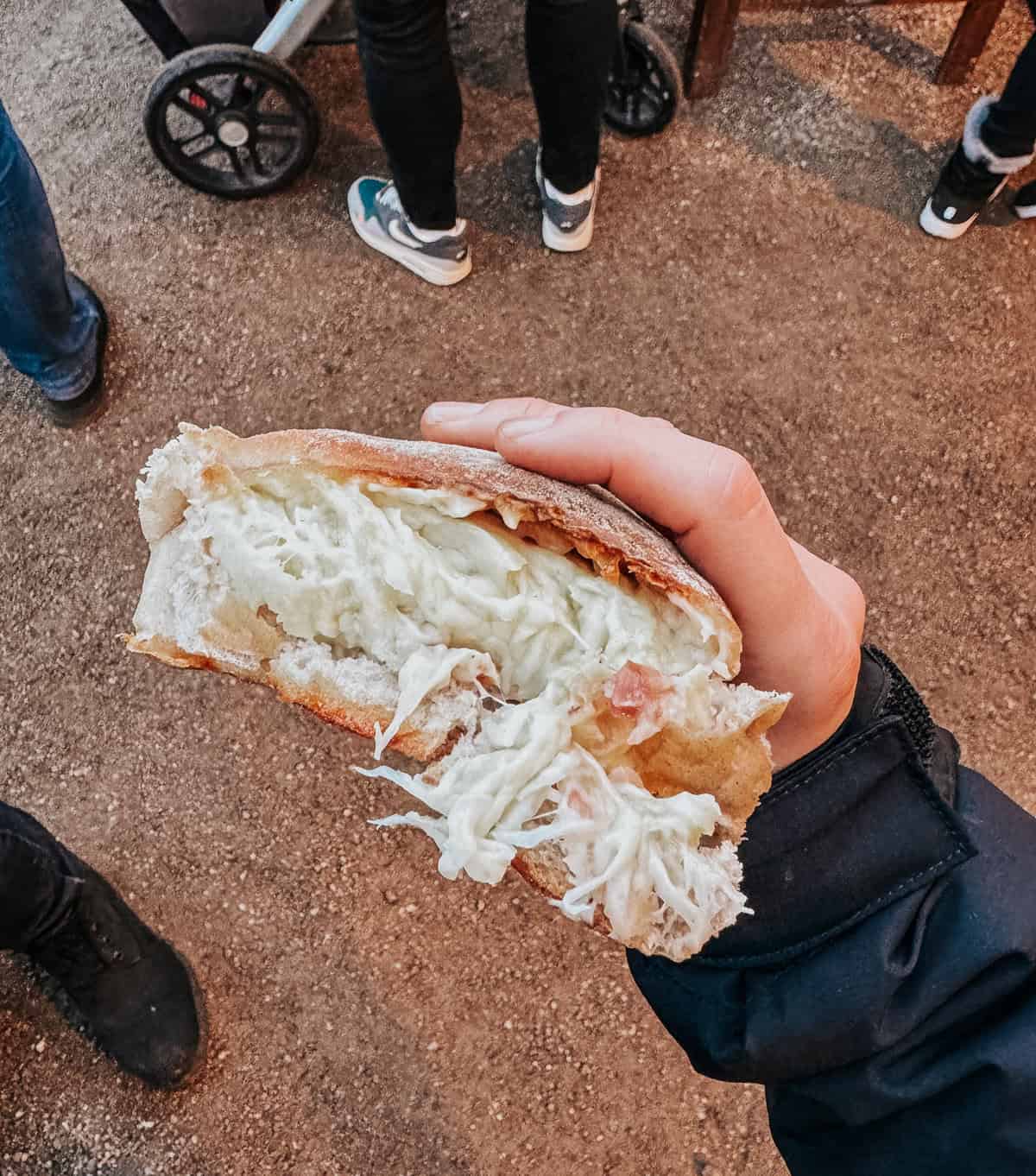 A hand holding a Handbrot, a German street food consisting of bread filled with cheese and ham, showcasing the gooey cheese stretching with each bite.