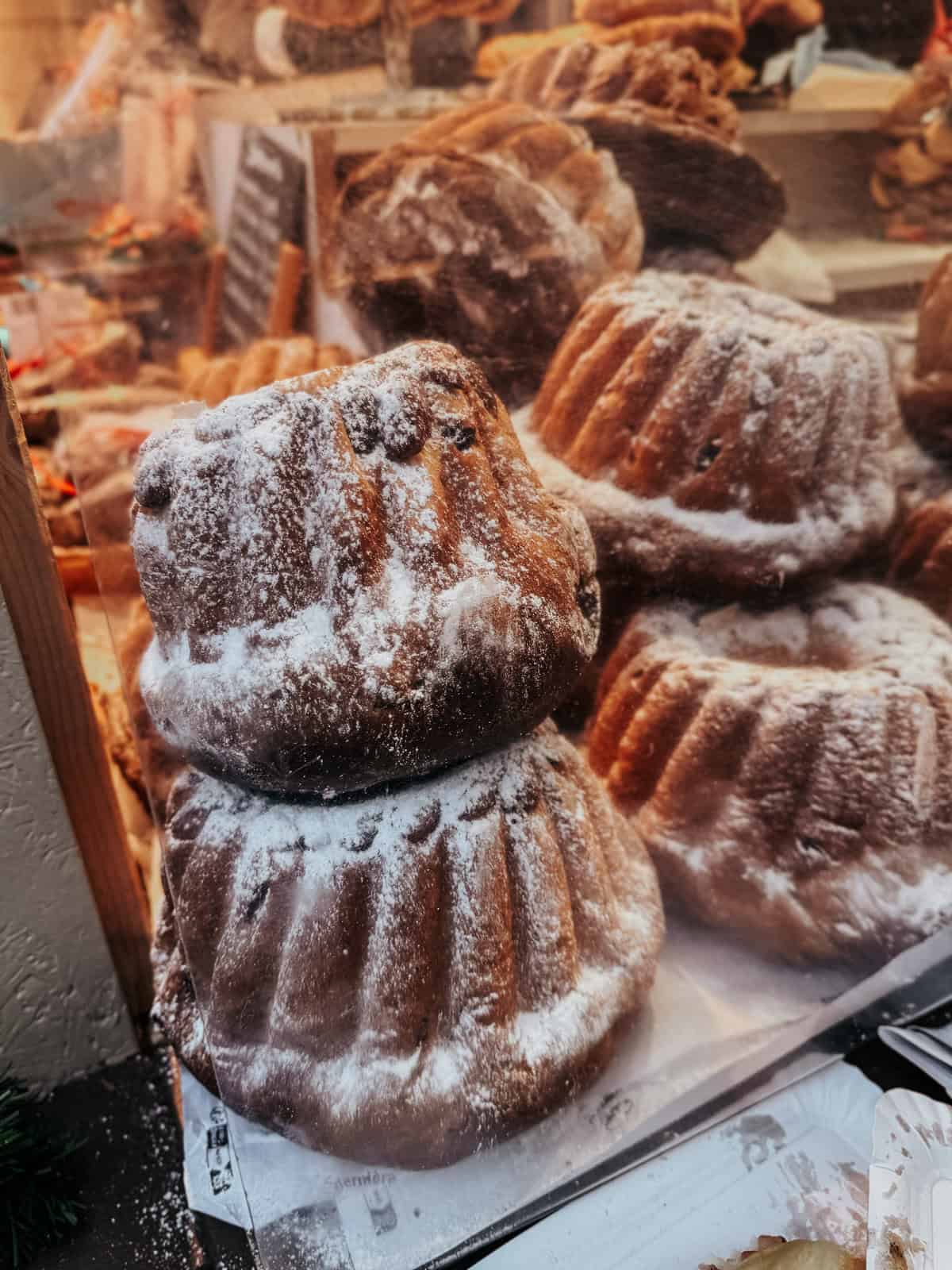 Several Alsatian Kouglofs dusted with powdered sugar stacked at a market, showcasing their distinctive circular, ridged shape