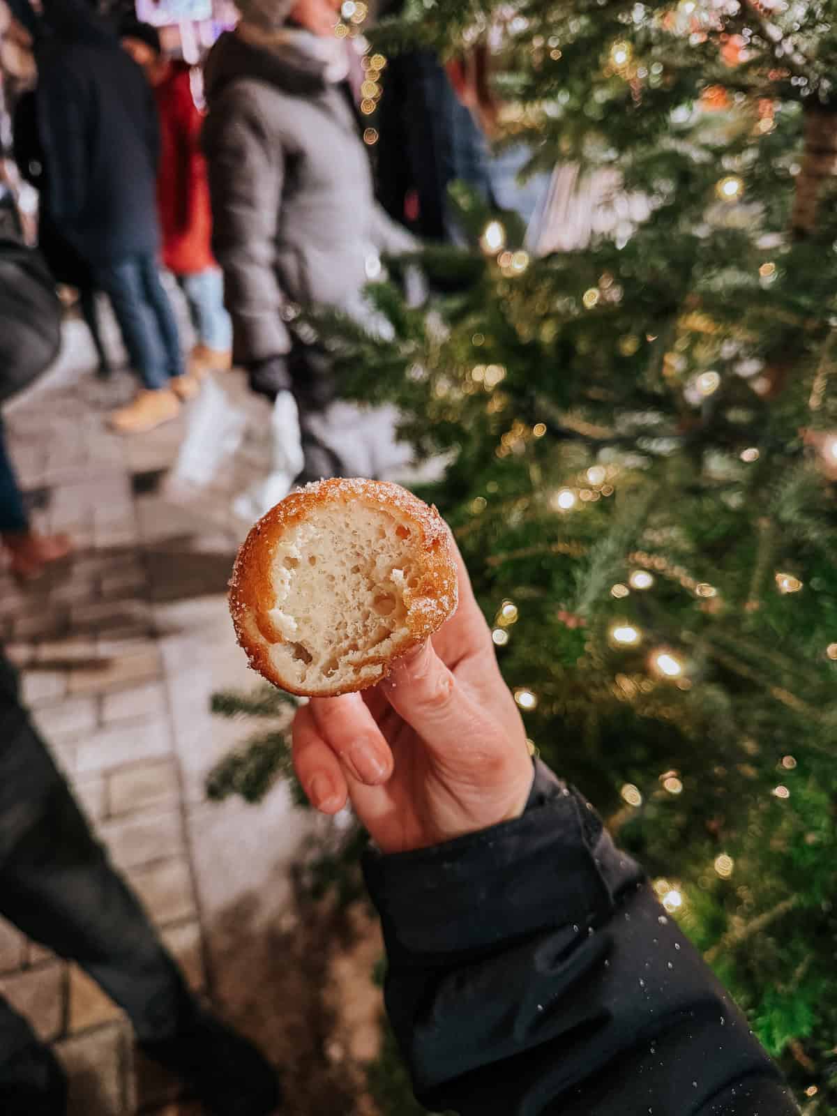 A close-up of a hand holding a bitten quark ball with the creamy filling visible, set against a festive backdrop of a decorated Christmas tree.