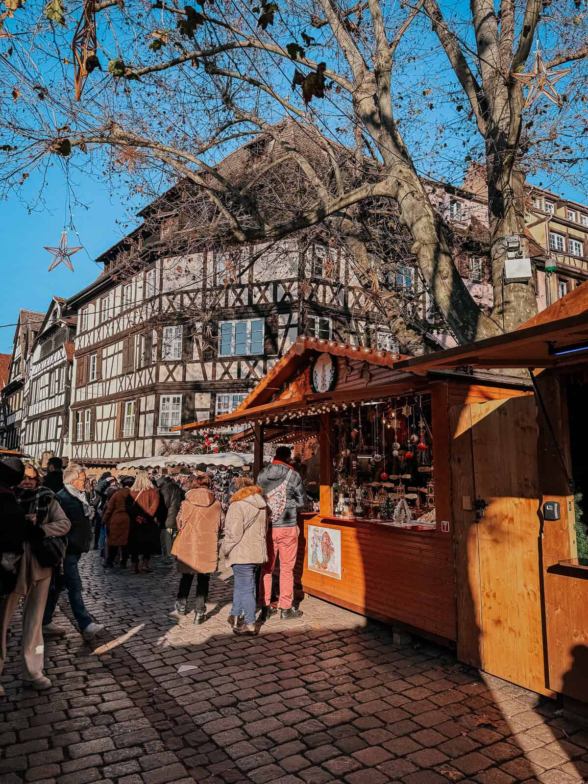 A vibrant and crowded Christmas market in a historic square, surrounded by traditional timber-framed buildings and festive decorations