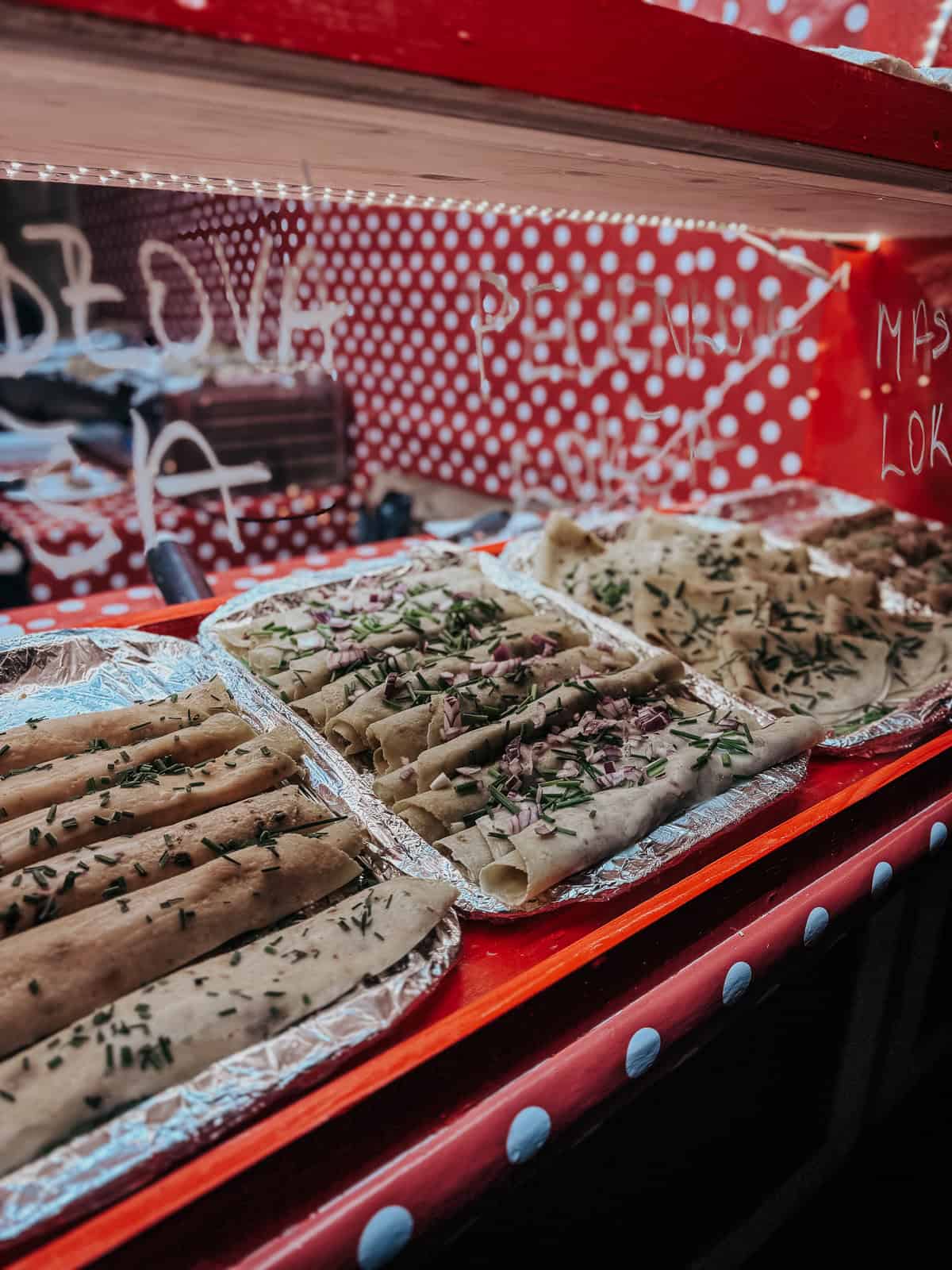 A close-up of a market stall displaying various traditional rolled pancakes garnished with herbs and onions.