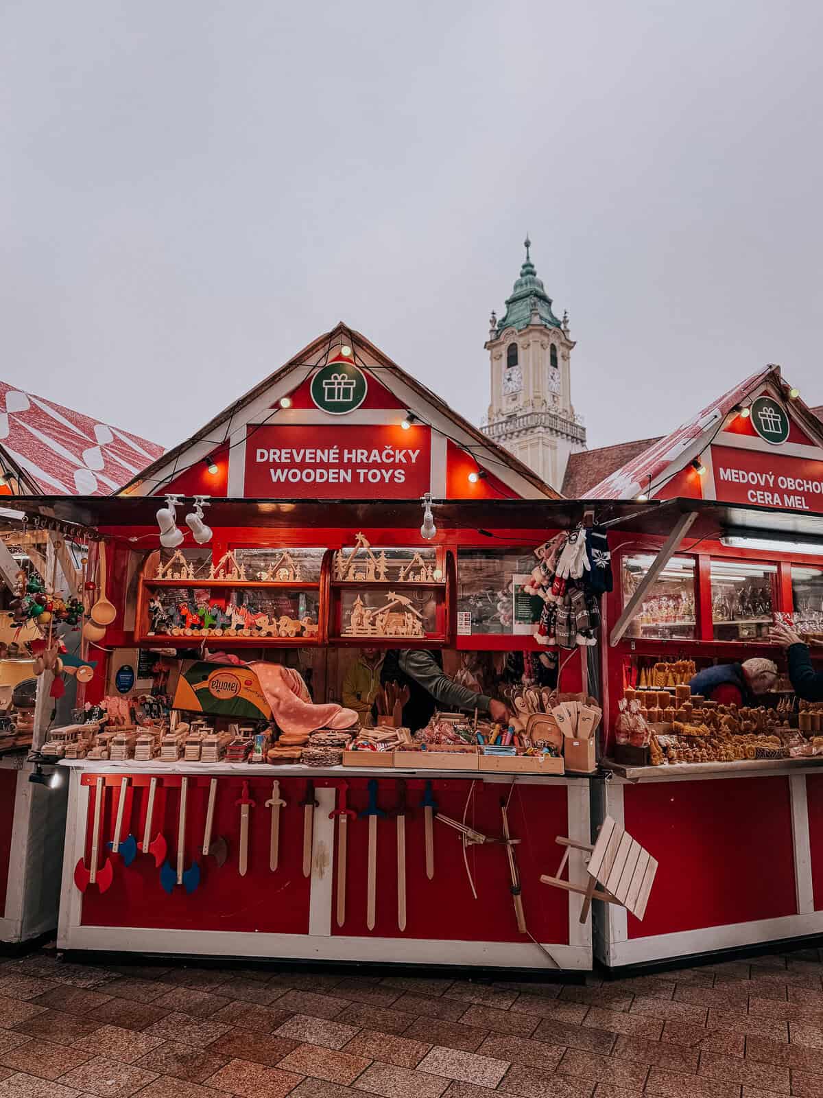 A festive market scene with wooden toy stalls, red roofs, and Christmas decorations, with a tower visible in the background.