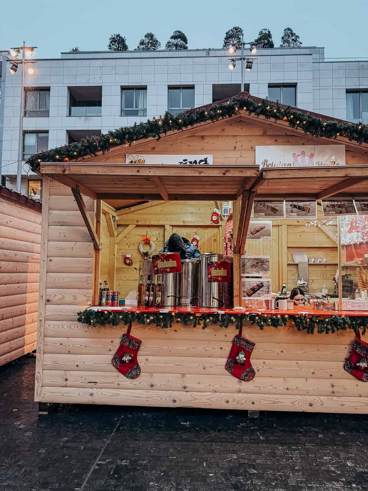 A decorated Christmas market stall selling hot beverages, adorned with festive garlands and stockings, under the soft glow of string lights.