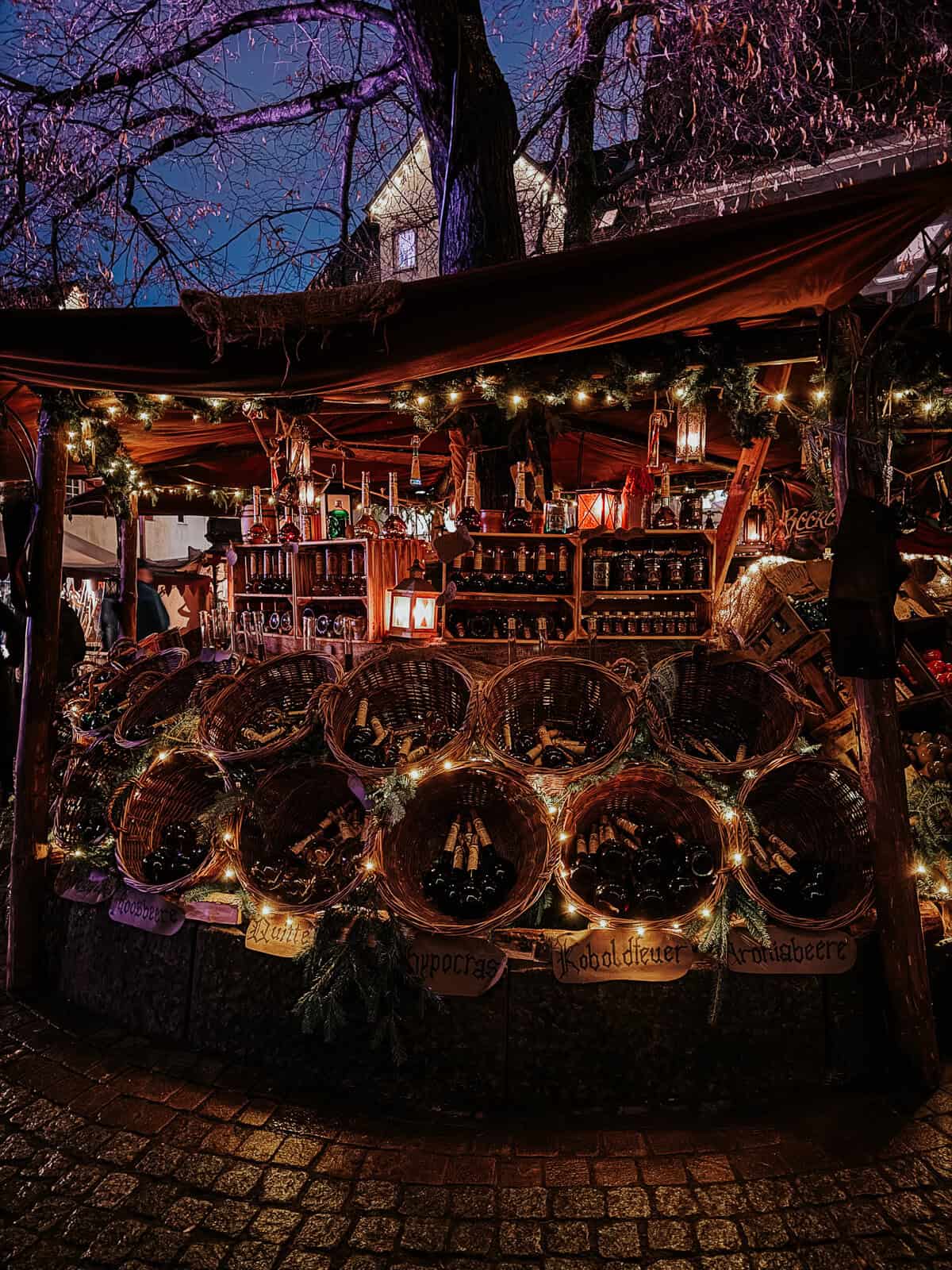 a nighttime view of a market booth beautifully illuminated with lights and decorated with Christmas greens and rustic elements.