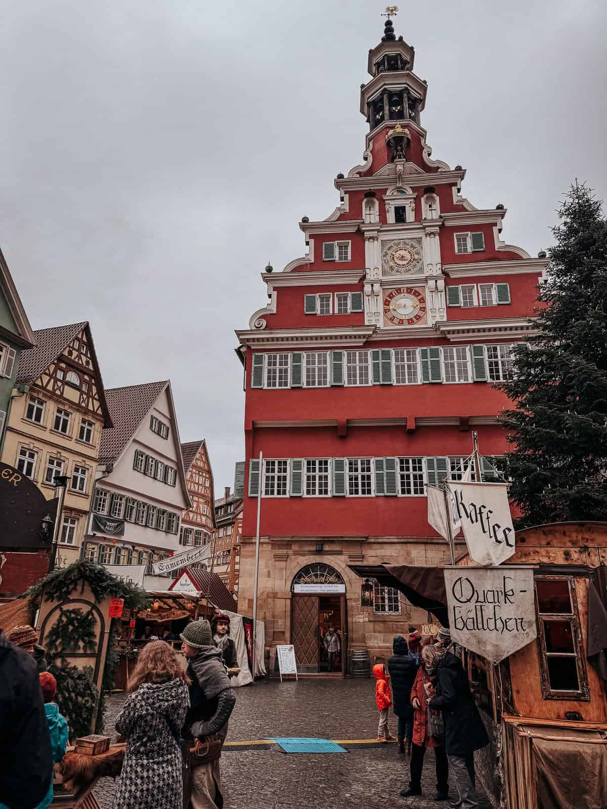 Esslingen's old town hall, a striking red building with a prominent clock tower, surrounded by timber-framed houses and a small market setup.