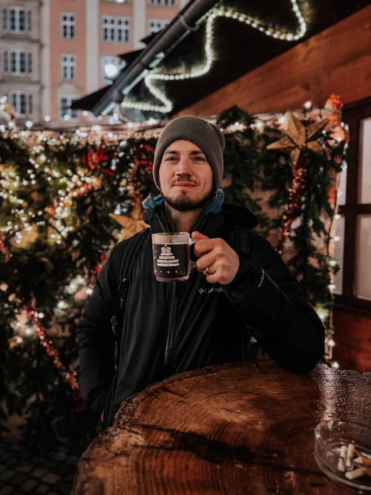 a man at a christmas market holding a glass of mulled beer