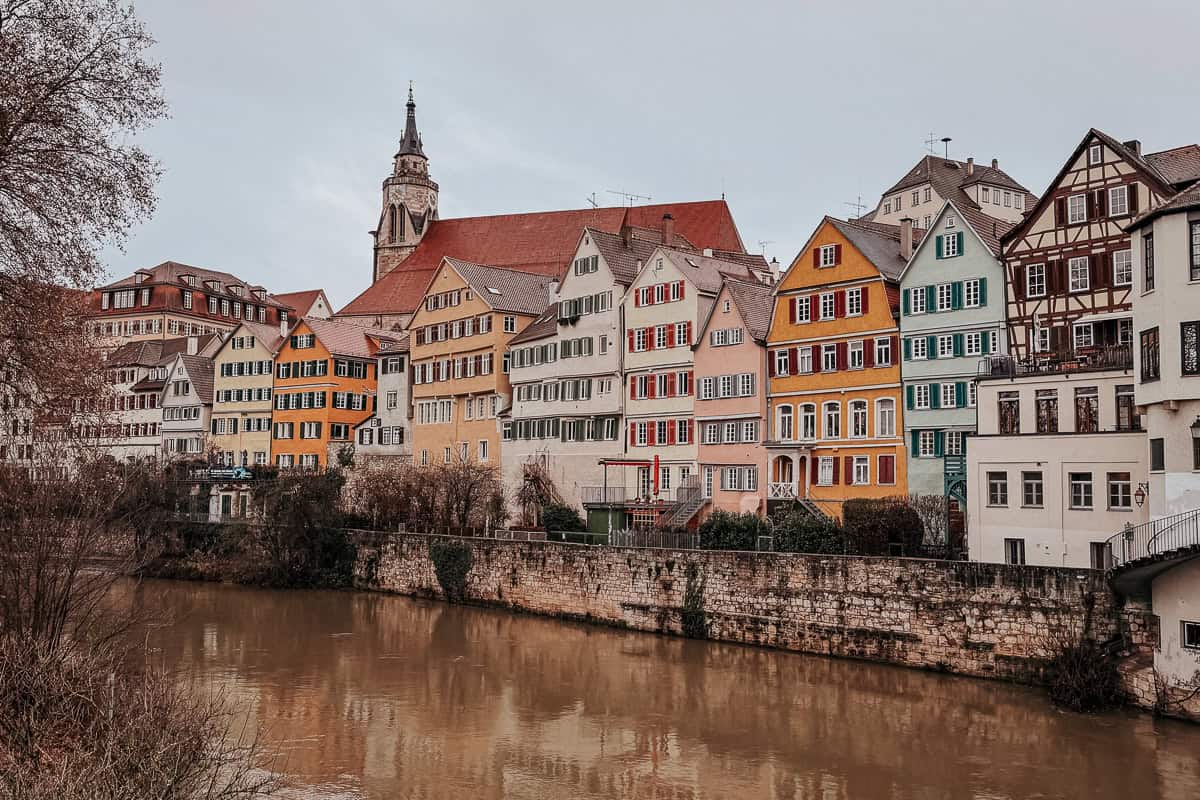 Panoramic view of colorful, multi-story buildings along the river in Tübingen, with reflections visible in the water