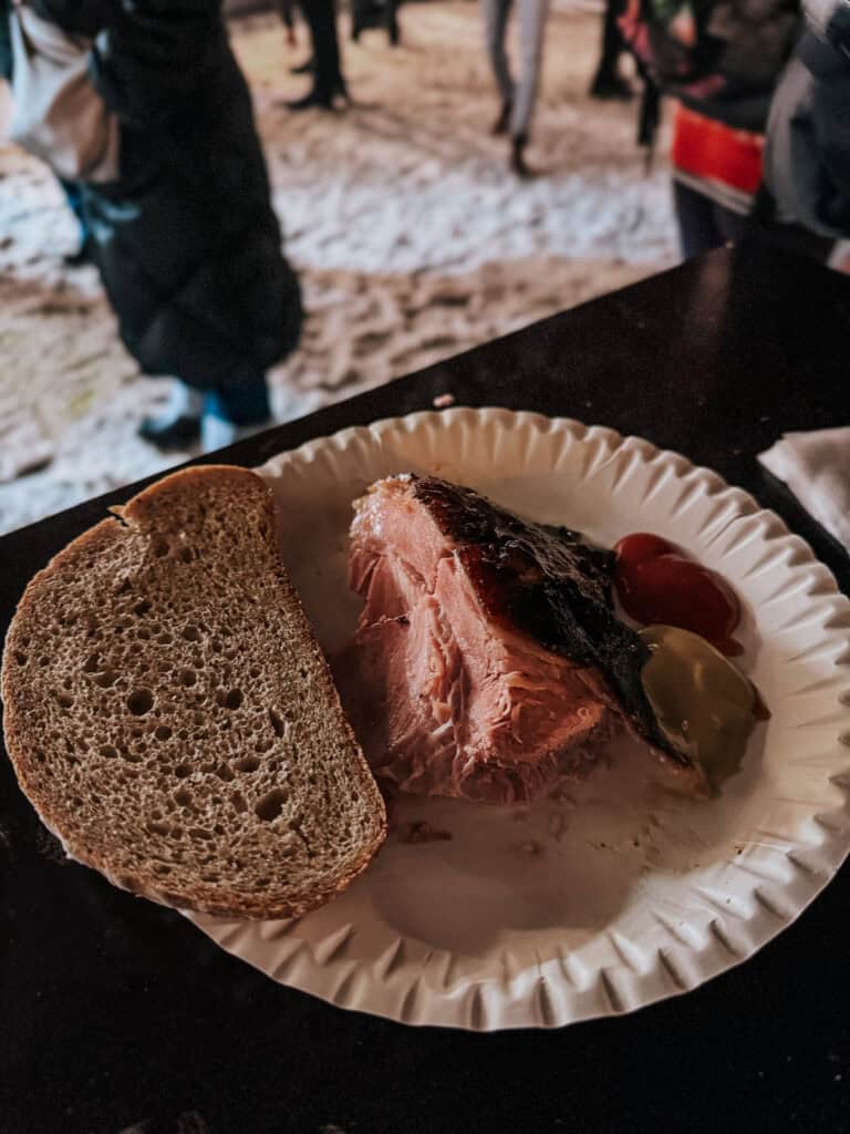 A large hunk of Prague ham with ketchup and brown bread on a white paper plate