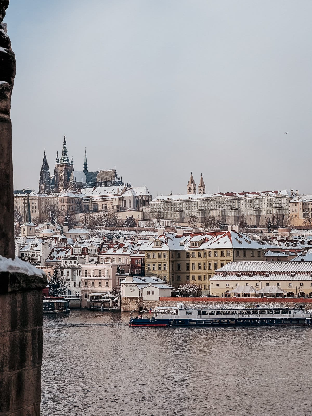 A view of the Prague river line with snow on the buildings and Prague castle in the background