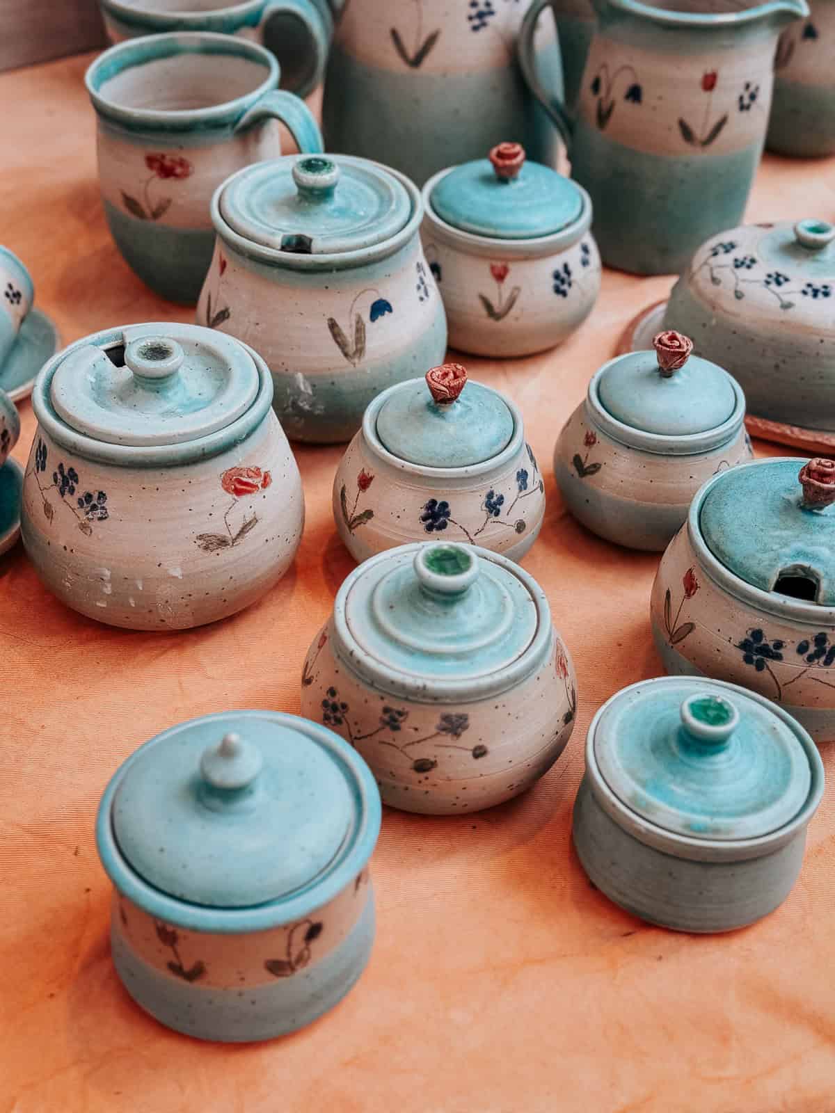 Variety of handcrafted ceramic pots displayed on a table, featuring light blue and sandy glazes with delicate floral designs