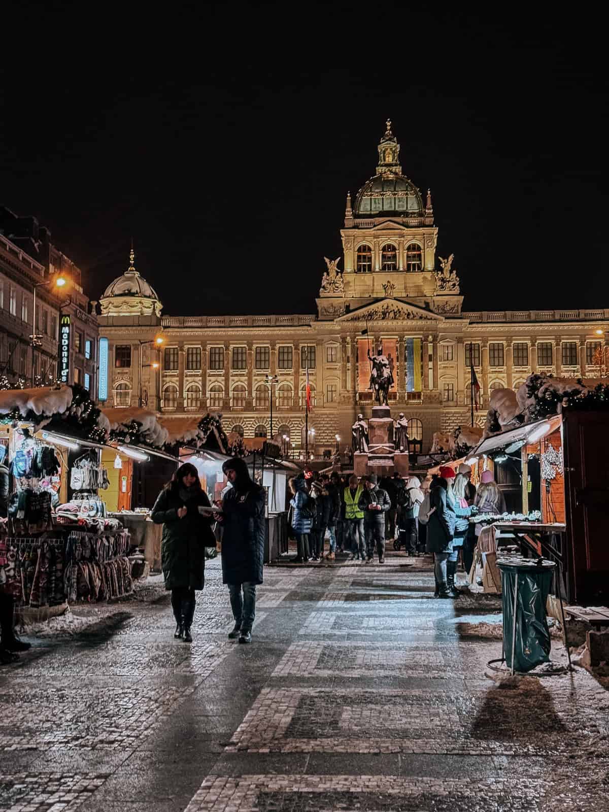 The Christmas market in front of the national musuem in Prague lit up at night with wooden market stalls