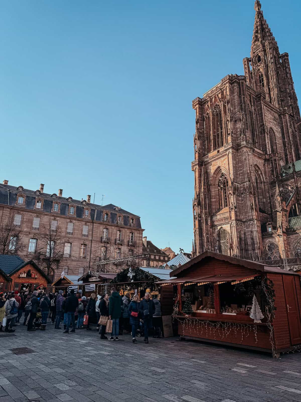 A close view of an elaborate Gothic cathedral next to a Christmas market, showcasing detailed architecture and festive market activity.