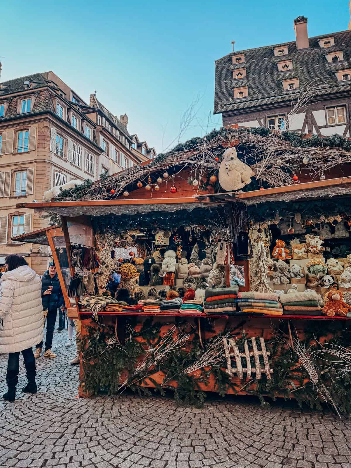 A vibrant Christmas market set in a square with the St. Thomas church in the background, featuring traditional stalls and a lively crowd.
