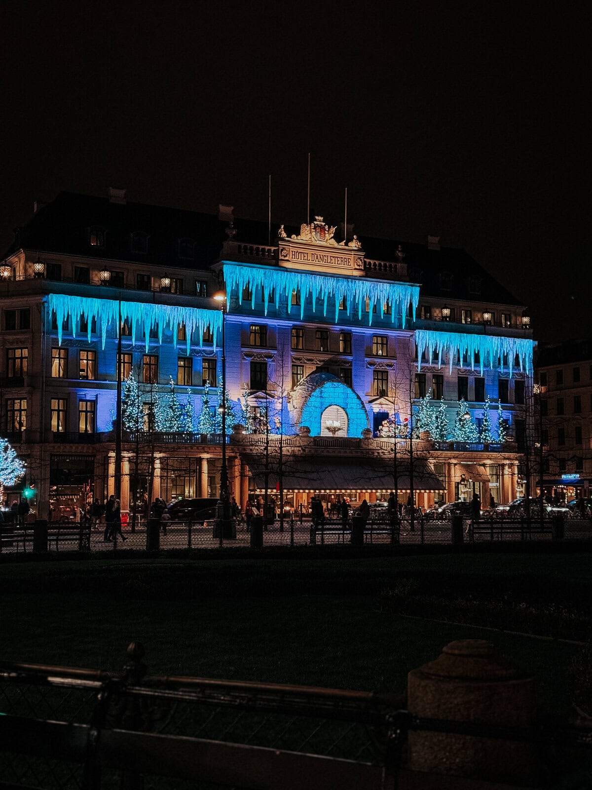 The Hotel D'Angleterre in Copenhagen lit with vibrant blue lights and ice-like decorations under a winter night sky, enhancing its grandeur and festive spirit.