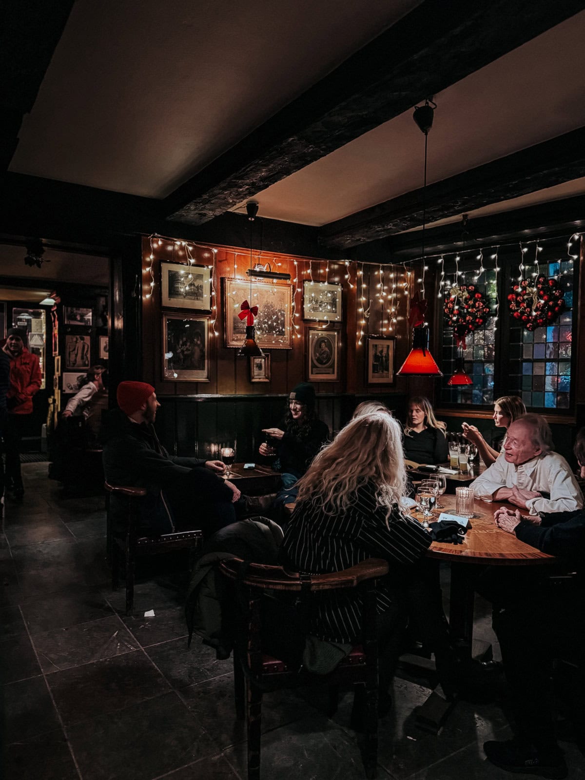 An atmospheric pub scene decorated with Christmas lights and vintage memorabilia on the walls, featuring patrons enjoying drinks and conversations at wooden tables