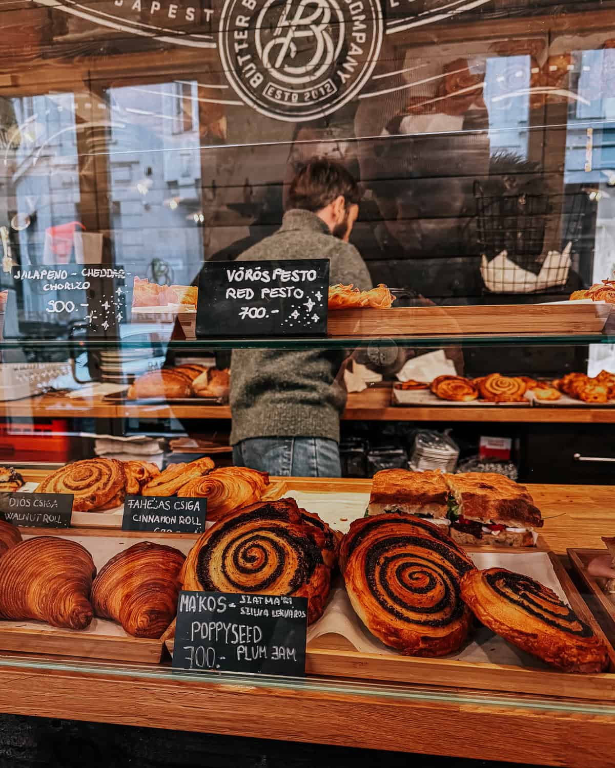 A plate filled with croissants generously stuffed with green filling, displayed under a bakery's glass case.