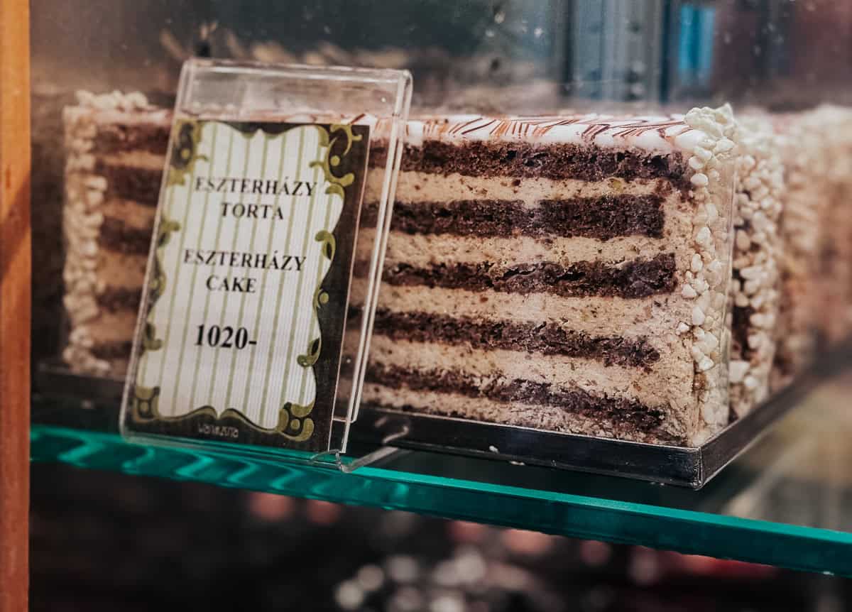 Close-up of Esterhazy Torte slices displayed in a bakery case, with a sign indicating the name of the cake and its price as 1020