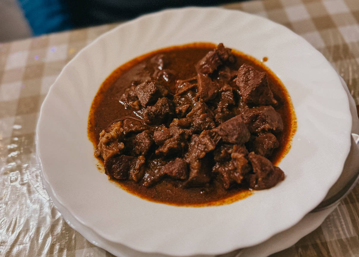 A plate of hearty stew with chunks of meat in rich brown sauce served on a white plate.