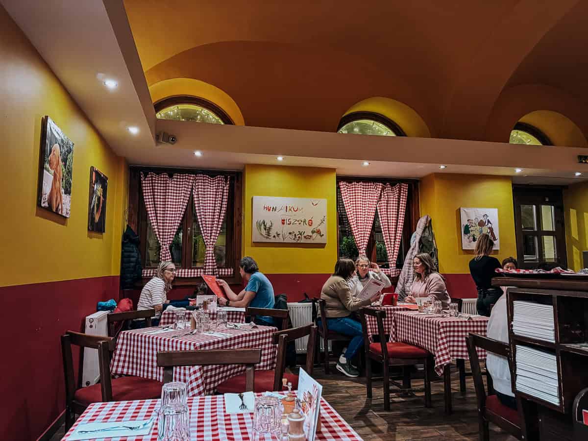 An interior view of a cozy restaurant with red and white checkered tablecloths, yellow and red walls, and customers sitting at tables.