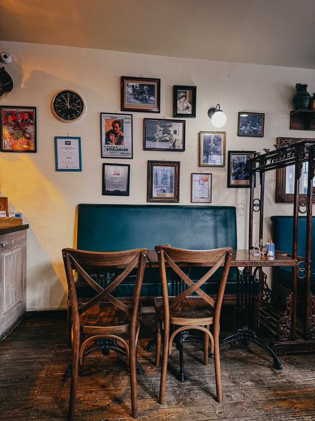 Interior of a café with wooden chairs and a wall decorated with framed pictures and a clock.