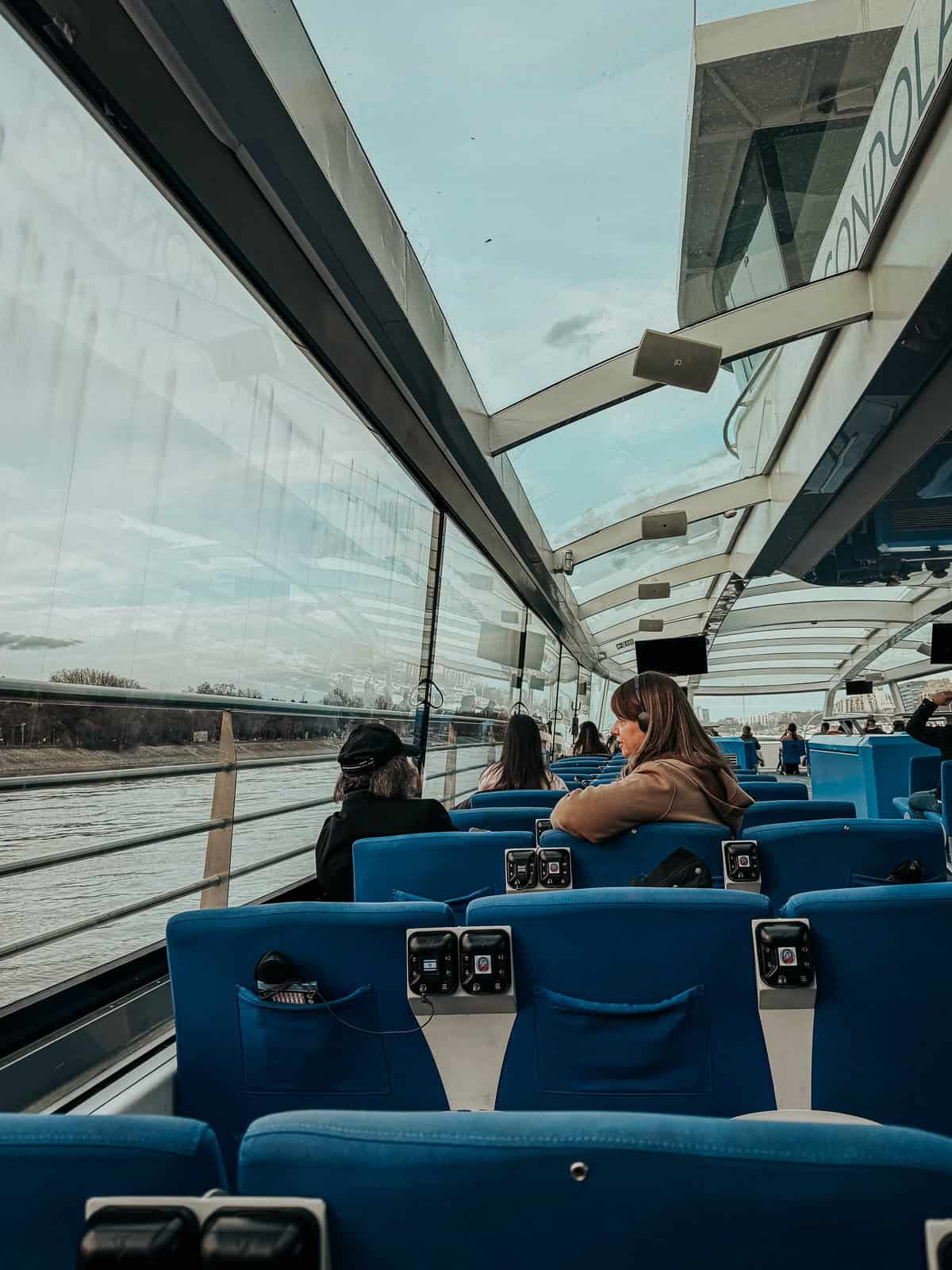 the inside of a boat with glass walls and blue seats with a woman looking out the window