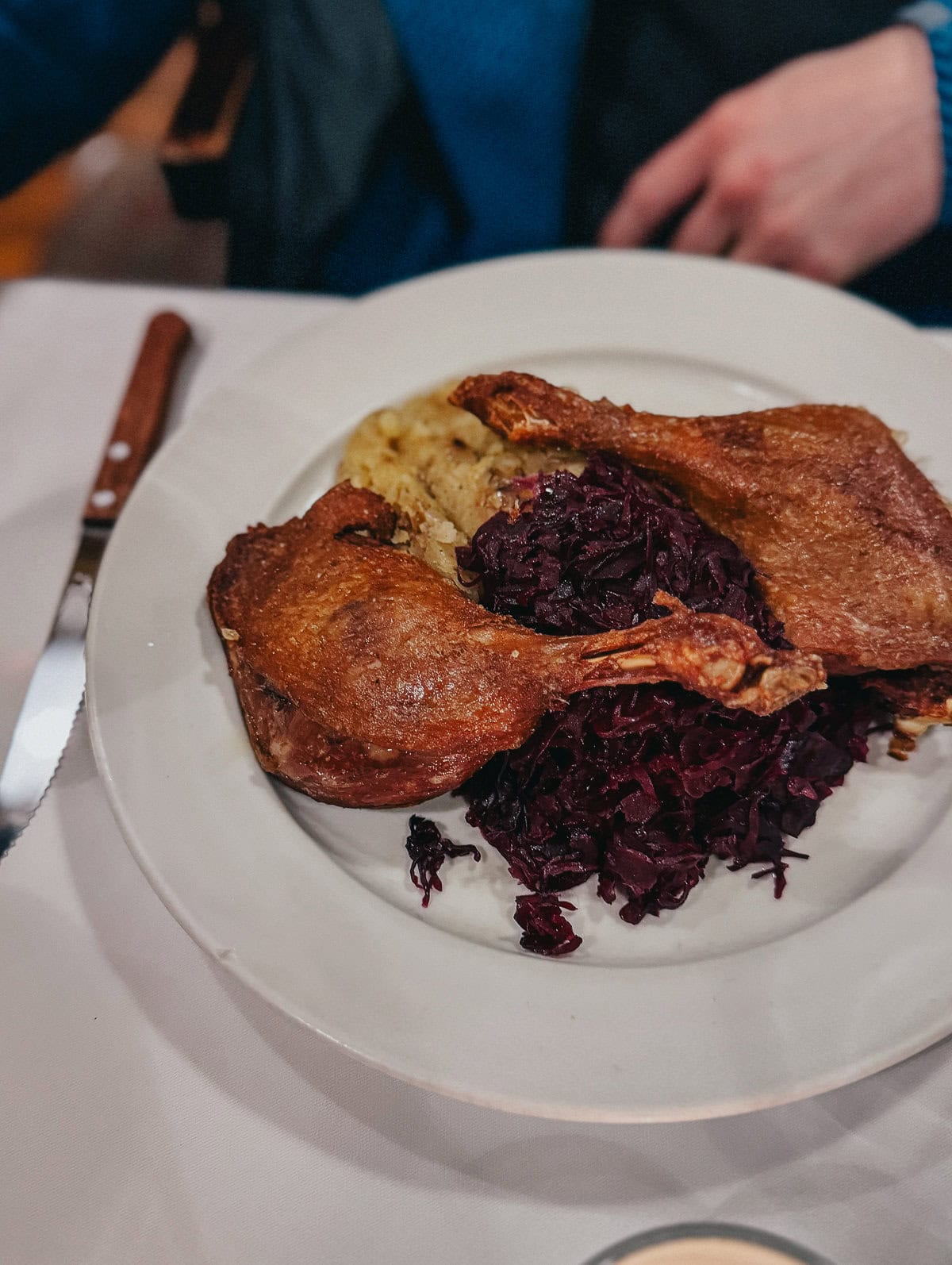 A plate of roasted duck legs served with red cabbage and potatoes, ready to be enjoyed in a restaurant setting.