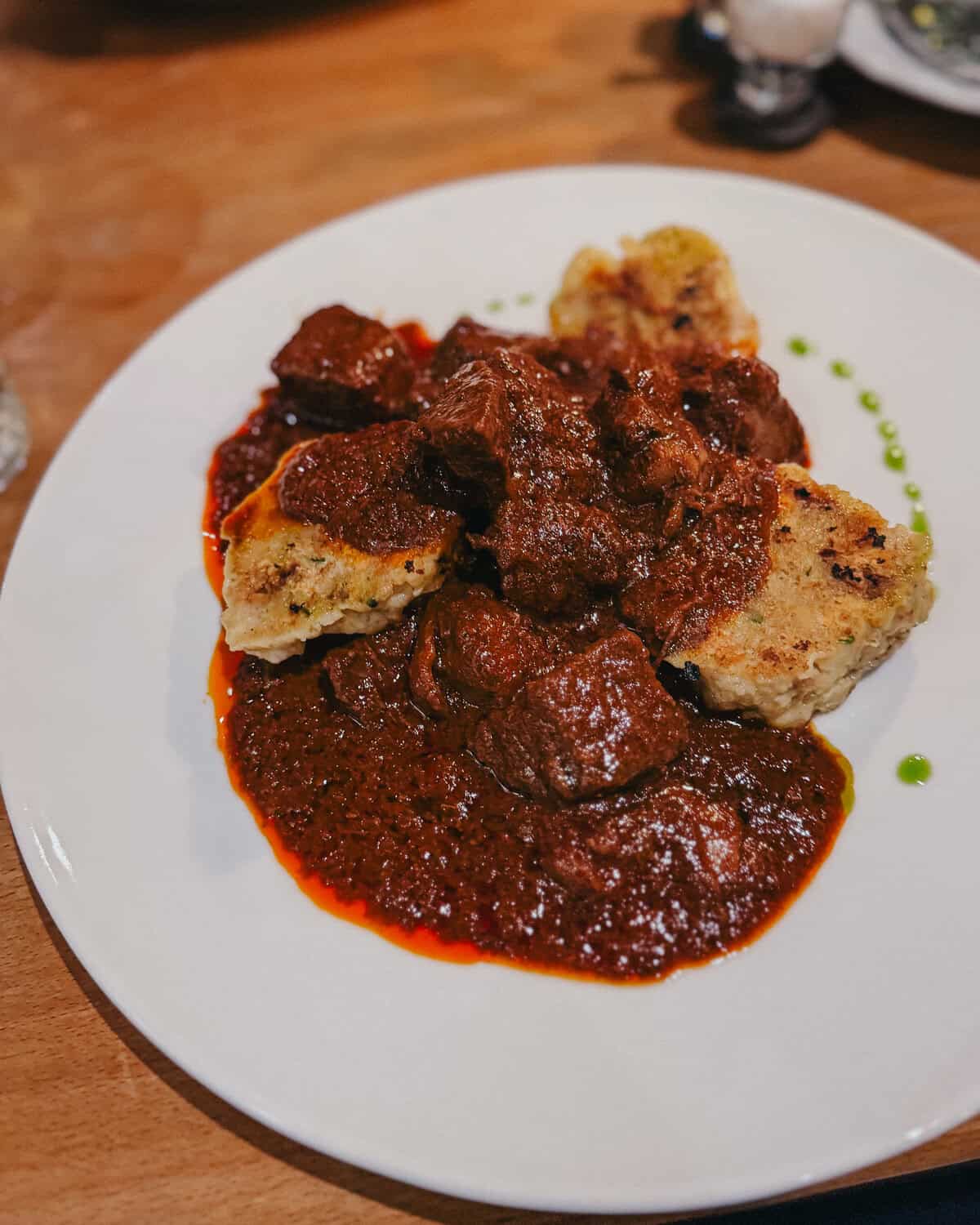 A close-up of a dish featuring chunks of beef in a rich, red sauce served with bread dumplings.