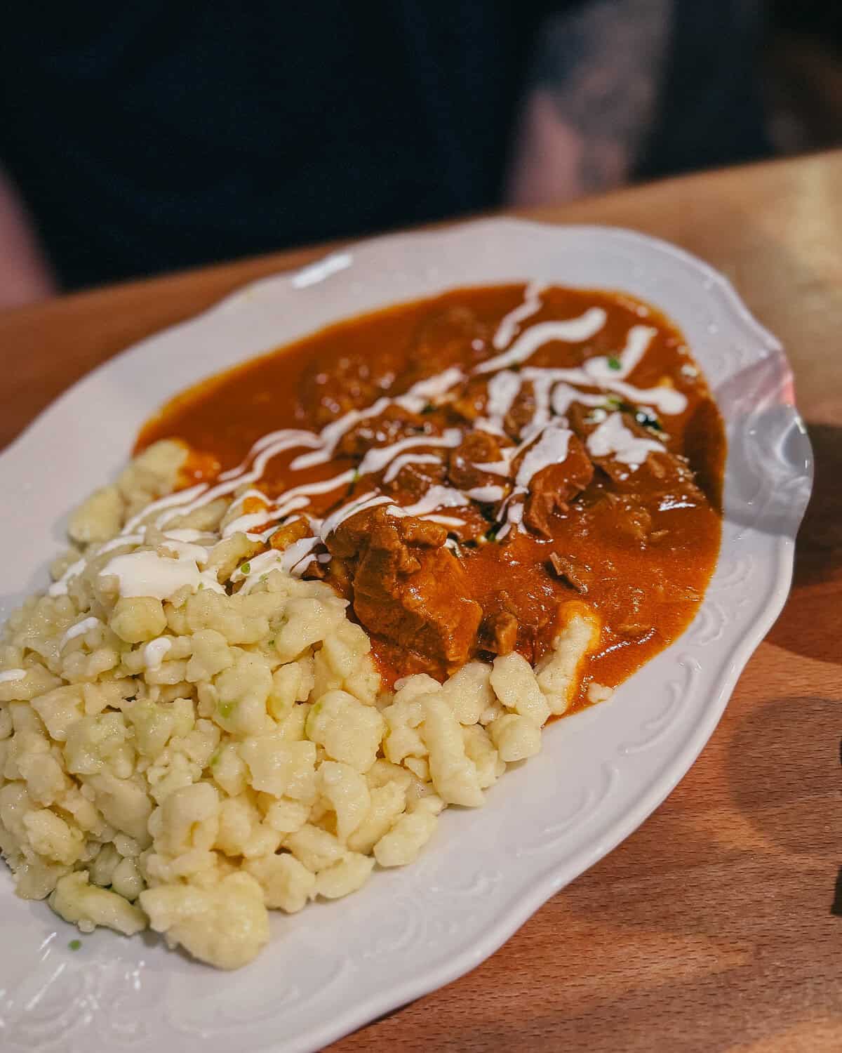 A plate of Hungarian food with a creamy sauce, chunks of meat, and a side of dumplings drizzled with sour cream.