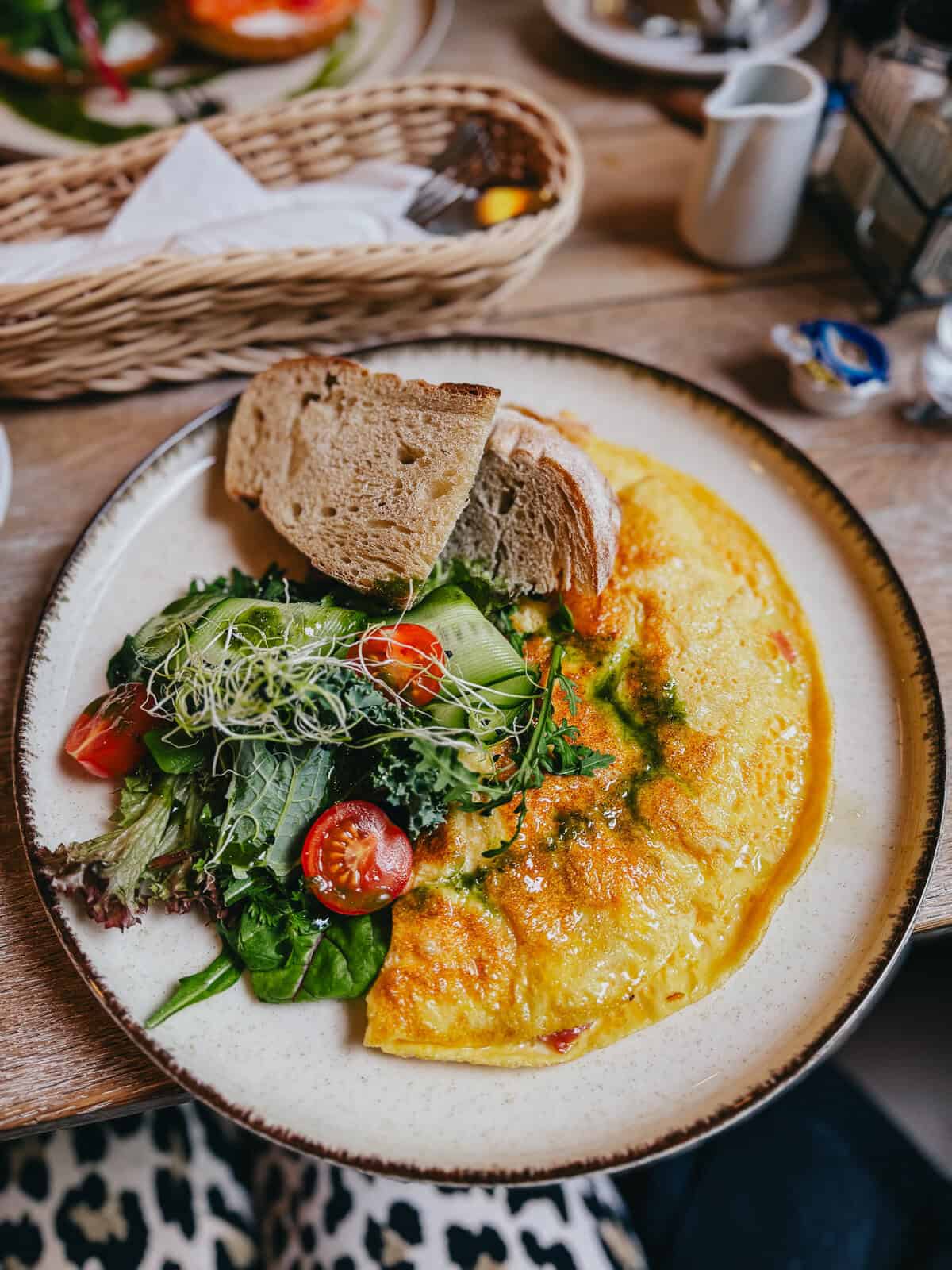 A plate of omelet with a side salad and slices of bread, served on a rustic table.