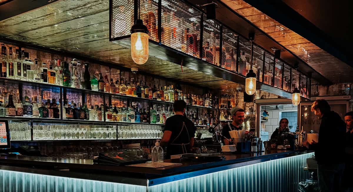 A well-stocked bar with a variety of spirits and a warm, inviting atmosphere, featuring bartenders serving drinks.