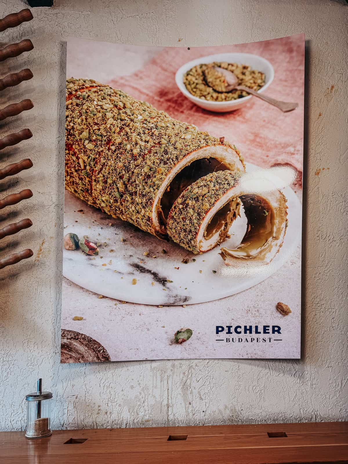 a sign that says Pichler with a chimney cake coated in pistachios on it