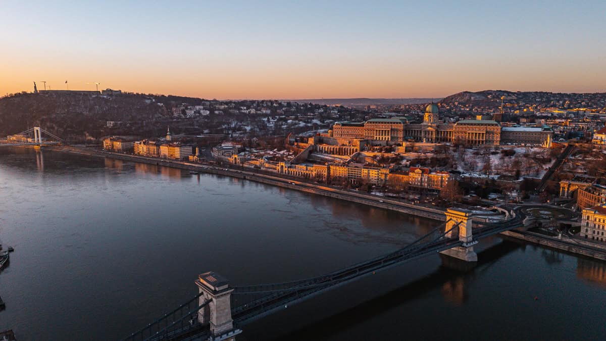 Aerial view of the Hungarian Parliament Building at sunrise, situated along the Danube River with the cityscape of Budapest in the background