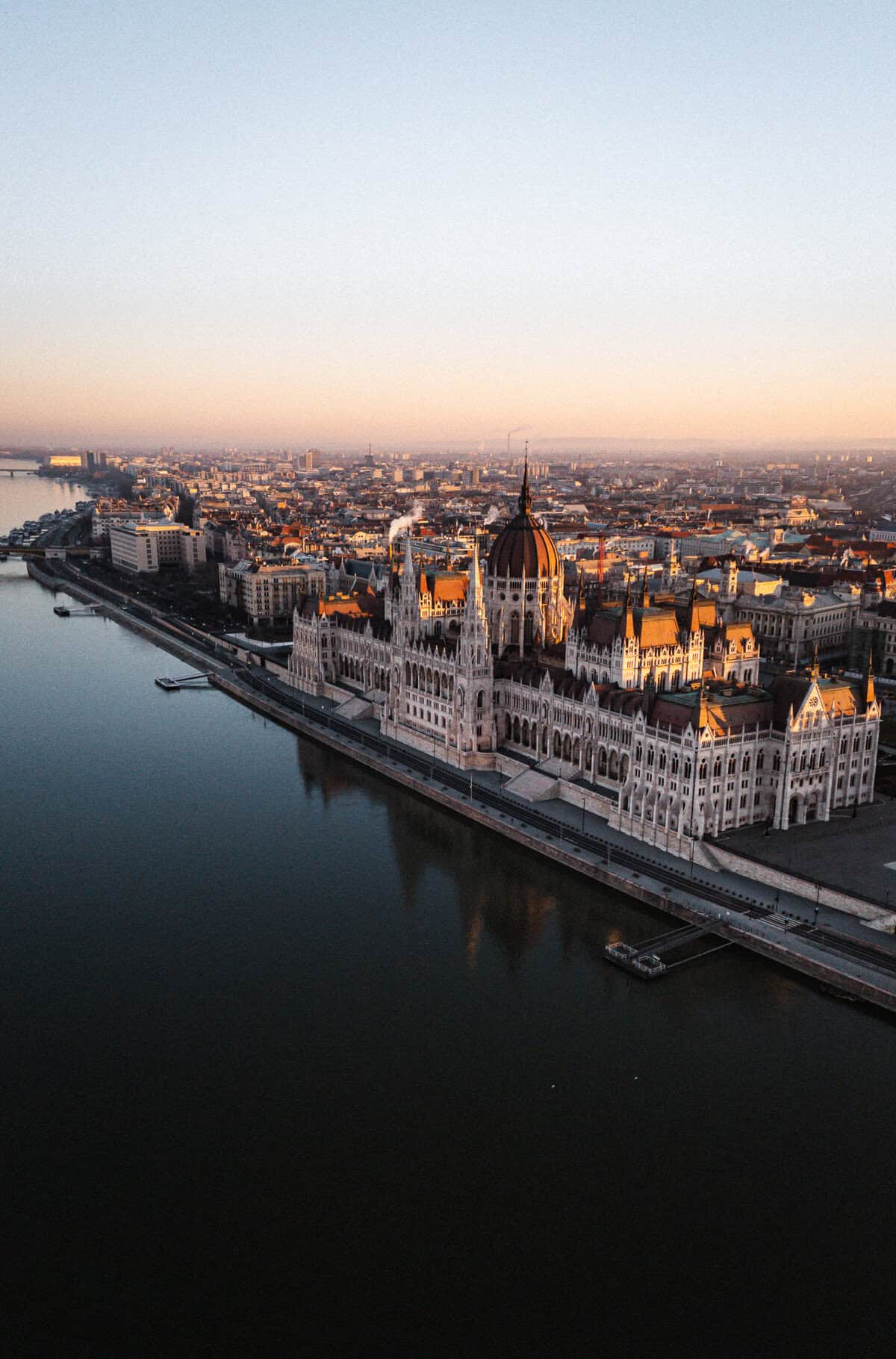 Aerial view of Budapest at sunset, featuring Buda Castle and the surrounding landscape with the Danube River in the foreground.