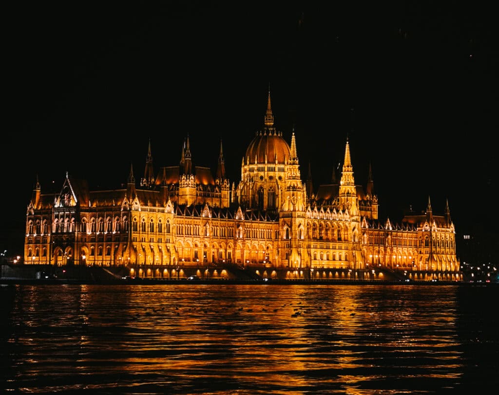 The Hungarian Parliament Building illuminated at night, reflecting off the calm waters of the Danube River in Budapest.