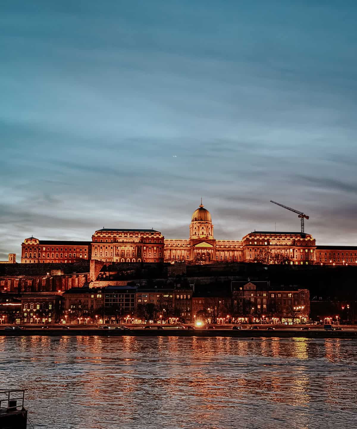 The Buda Castle in Budapest lit up beautifully at night, with its reflection shimmering on the Danube River.