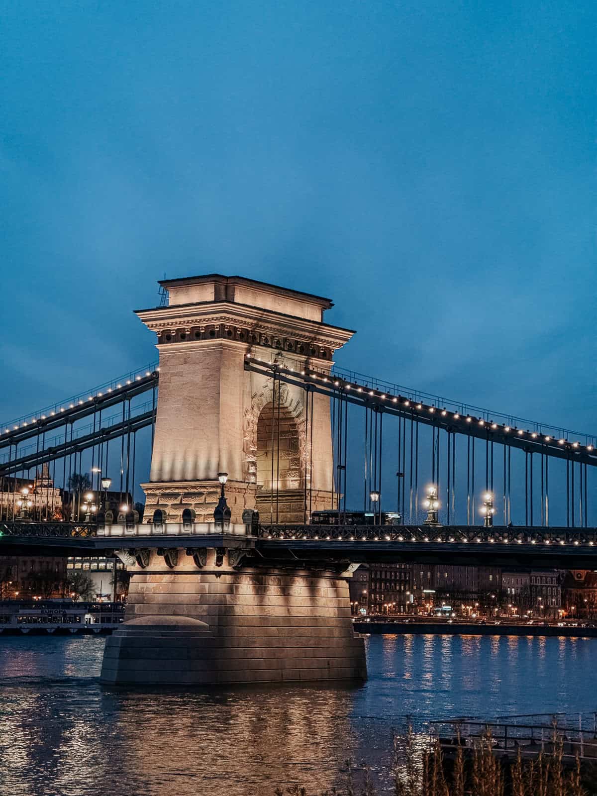 The Széchenyi Chain Bridge illuminated at night, spanning the Danube River in Budapest with city lights reflecting on the wate
